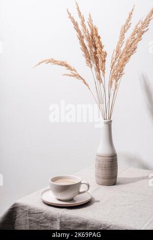 Une tasse de café et un vase avec de l'herbe de pampas sur une table avec nappe. Encore la vie. Banque D'Images