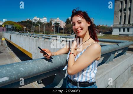 Une jeune femme à tête rouge vérifiant des messages sur son téléphone cellulaire, attitude souriante. Copier l'espace. Orientation paysage. Banque D'Images