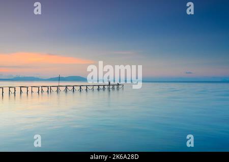 Bajau enfants pêchant sur le pont abandonné pendant le coucher de soleil pastel à Île Mabul Banque D'Images