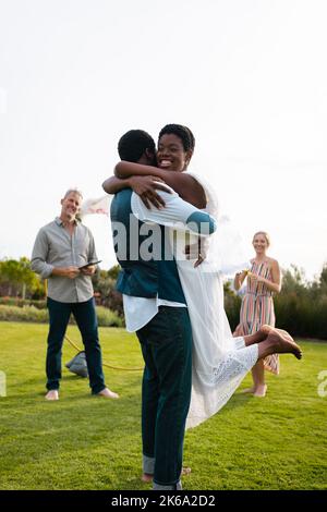 Couple afro-américain heureux avec des amis caucasiens embrassant pendant le mariage Banque D'Images