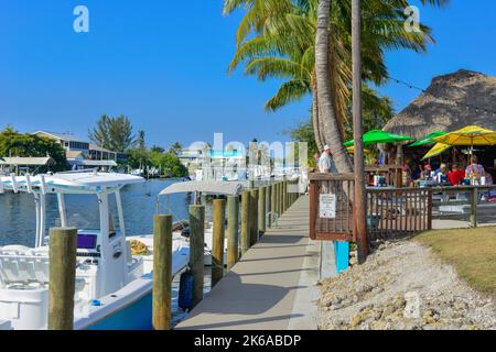 Vue sur les canaux avec bateaux à quai, à côté du restaurant et bar Phuzzy's Boat Shack avec toits de chaume et dîner en plein air à St. James City, FL, Banque D'Images