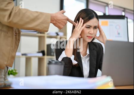 Une jeune femme d'affaires ou une employée de l'entreprise asiatique, stressée et frustrée, se trouve à son bureau, se confortant mal à son patron pendant qu'elle travaille Banque D'Images