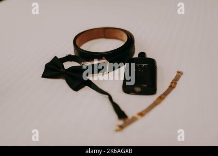 Un noeud papillon noir, ceinture, et bracelet doré isolé sur fond blanc, accessoires pour le marié Banque D'Images