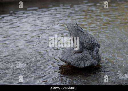 La fontaine de grenouille en pierre satute craque l'eau de l'embouchure dans un parc Banque D'Images