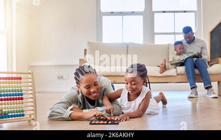 Fille afro-américaine jouant avec un abacus et d'autres jouets tout en étant couché sur le sol avec sa mère. Jeune fille liant avec sa mère. Sourire Banque D'Images
