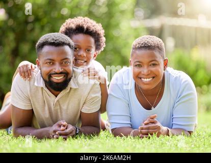 Prendre un peu de soleil pendant les saisons ici. Portrait d'une famille heureuse se détendant ensemble sur la pelouse à l'extérieur. Banque D'Images