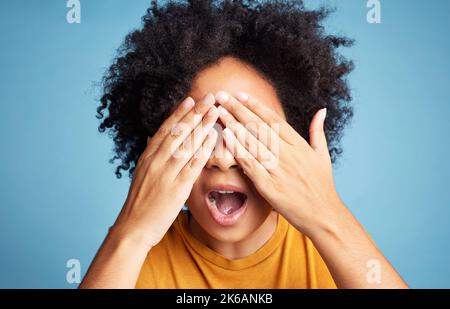 Je ne peux pas regarder. Une femme méconnaissable se tenant sur un fond bleu dans le studio et couvrant ses yeux avec ses mains. Banque D'Images