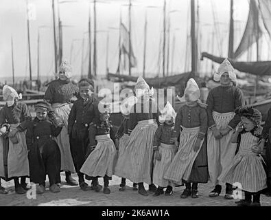 Un groupe d'enfants en vêtements traditionnels sur un quai aux pays-Bas c. 1930. Les costumes traditionnels varient selon la couleur et le design dans les 12 provinces néerlandaises – les similitudes incluent la robe à manches longues et le tablier de base portés par les femmes et les vêtements de travail rustiques portés par les hommes. Les vêtements pour enfants sont d'un design similaire – une photographie vintage 1920s/30s. Banque D'Images