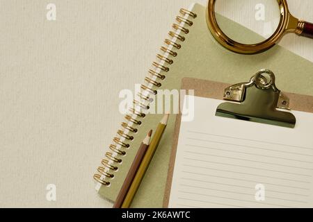 Carnet vert, presse-papiers, crayons de couleur, loupe sur le bureau. pose à plat, vue du dessus, espace pour copier Banque D'Images