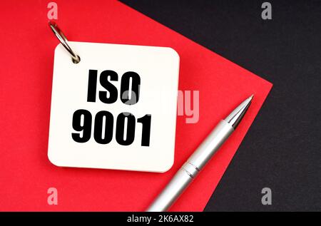 Concept d'industrie et d'entreprise. Sur un fond noir et rouge se trouve un stylo et un carnet avec l'inscription - ISO 9001 Banque D'Images