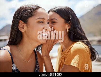 Une amie est ce dont le cœur a besoin tout le temps. Une jeune femme chuchote dans l'oreille de ses amis tout en traînant ensemble dehors. Banque D'Images