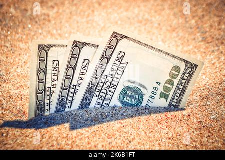 Les dolars d'argent à moitié couverts de sable se trouvent sur la plage de près. L'argent sort du sol. Billets de dollars partiellement enterrés dans le sable sur mer océan concept de plage finance argent vacances détente vacances. Banque D'Images