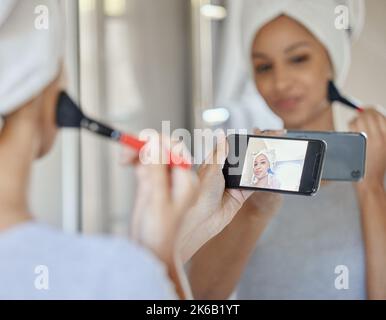 La lumière s'améliore ici. Une jeune femme s'enregistrant elle-même appliquant le maquillage à la maison. Banque D'Images