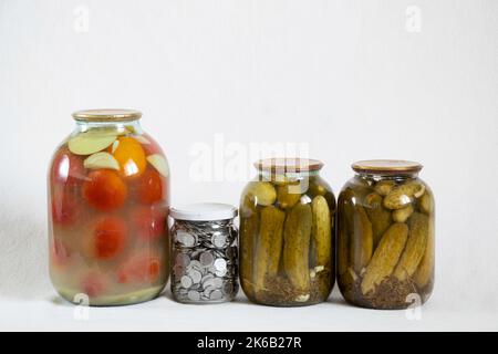 Tomates en conserve et concombres en pots et à côté d'une banque avec des kopecks ukrainiens sur fond blanc, économiser de l'argent dans une banque, des finances et de la nourriture Banque D'Images