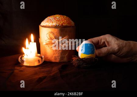 Gâteau de Pâques et à côté d'un oeuf avec un drapeau peint de l'Ukraine dans les mains d'une femme sur fond noir, bougies, vacances de Pâques en Ukraine pendant Banque D'Images