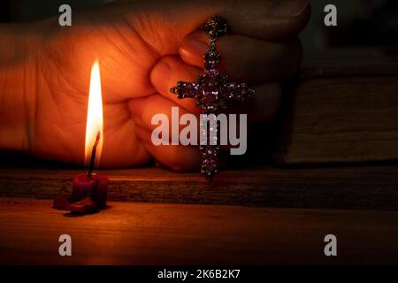 Une femme tient une croix près d'une bougie et d'une bible dans l'obscurité, une femme prie, priant, foi et religion, temple Banque D'Images