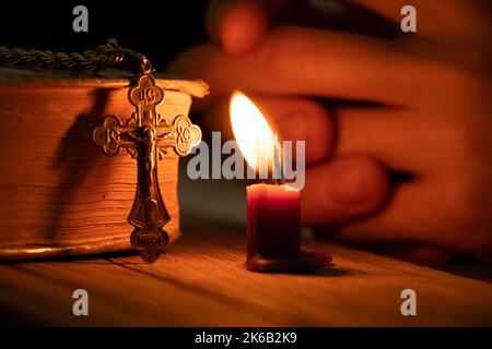 Une femme tient une croix près d'une bougie et d'une bible dans l'obscurité, une femme prie, priant, foi et religion, temple Banque D'Images