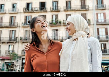 Des amies multi-ethniques se embrassent et rient tout en appréciant le temps ensemble à l'extérieur dans la rue. Banque D'Images