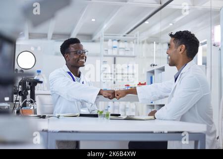 Deux scientifiques médicaux souriants assis ensemble dans un laboratoire et s'embuer. Professionnels de santé afro-américains et mixtes célébrant Banque D'Images