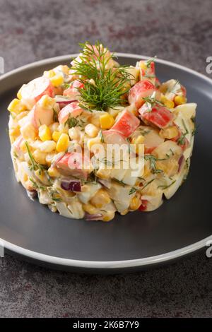 Délicieuse salade maison avec bâtonnets de crabe, maïs, oignon rouge, œufs durs et aneth dans l'assiette sur la table. Verticale Banque D'Images