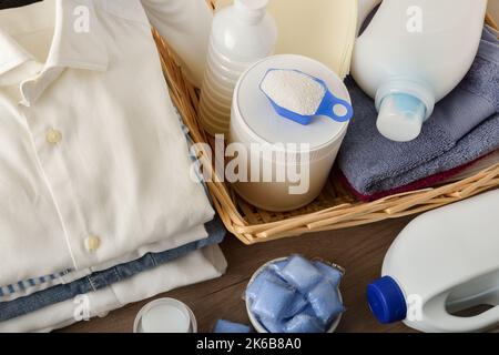 Détail des différents types de détergents à lessive sur une table en bois avec des vêtements blancs fraîchement lavés pliés. Vue en hauteur du dessus. Composition horizontale. Banque D'Images