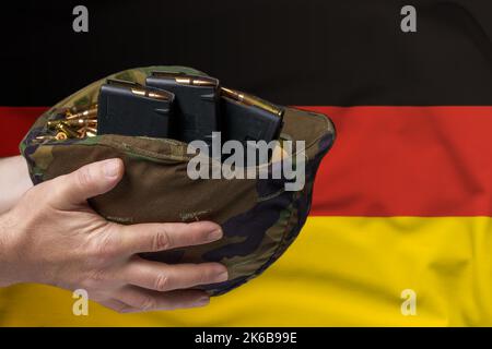 Un casque militaire avec cartouches et magazines pour un fusil dans les mains d'un homme sur le fond du drapeau de l'Allemagne. Le concept de Banque D'Images