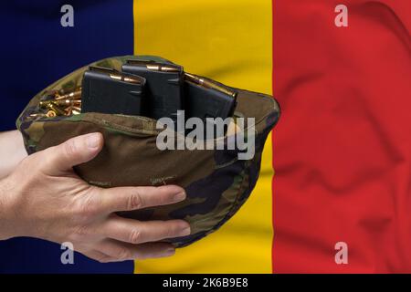 Un casque militaire avec cartouches et magazines pour un fusil dans les mains d'un homme sur le fond du drapeau de la Roumanie. Le concept de Banque D'Images