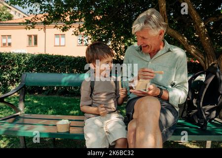 Un grand-père et un petit-fils heureux qui dégusseront des glaces tout en étant assis sur le banc Banque D'Images