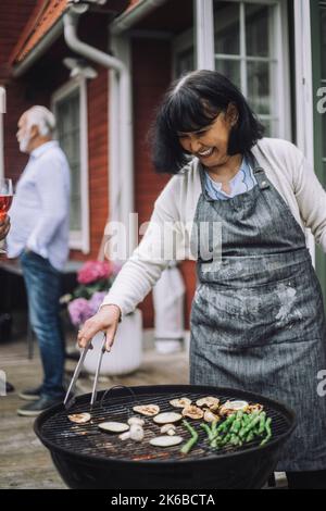 Bonne femme portant un tablier pour griller des légumes sur un barbecue lors de la fête Banque D'Images