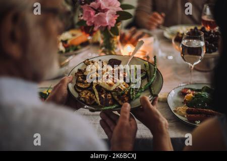 Homme passant la plaque alimentaire à la femme tout en étant assis à la table de salle à manger pendant la fête Banque D'Images