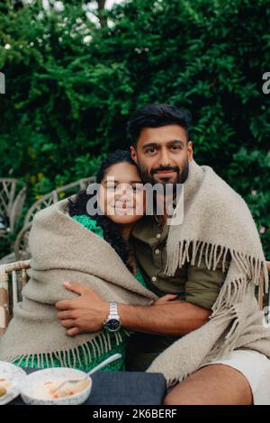 Portrait de l'homme et de la femme couverts dans une couverture s'embrassant en étant assis sur un banc Banque D'Images