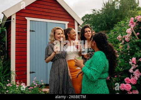 Des amies tiennent des boissons tout en discutant les unes avec les autres debout dans le jardin Banque D'Images