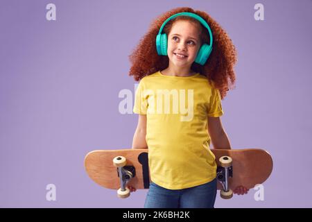 Photo de studio d'un casque de jeune fille tenant le skateboard sur fond violet Banque D'Images