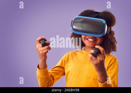 Photo de studio d'un garçon portant un casque de réalité virtuelle jeu avec contrôleur sur fond violet Banque D'Images