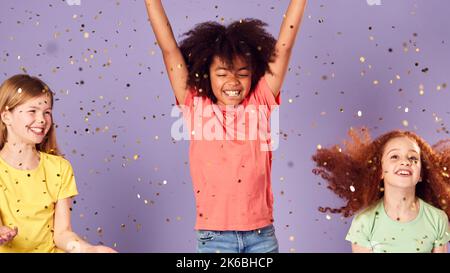 Photo en studio d'enfants avec saut de paillettes dans l'air avec bras étirés sur fond violet Banque D'Images