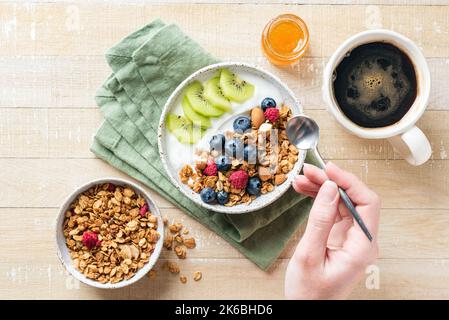 Bol de yaourt à la granola avec fruits et baies pour un petit déjeuner sain. Femme mangeant du granola avec du yaourt et des fruits Banque D'Images