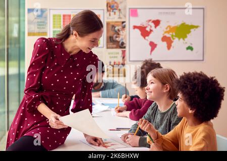 Femme souriante enseignante à l'école primaire travaillant au bureau en classe avec les élèves Banque D'Images