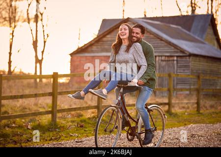 Couple à vélo à travers la campagne avec une femme assise sur le guidon Banque D'Images