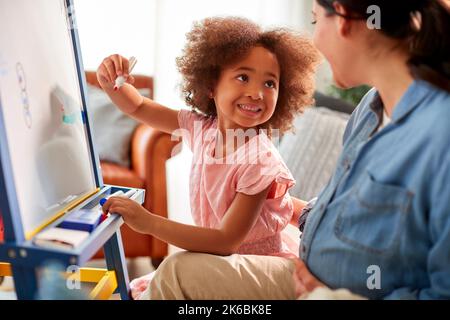 Mère et fille ayant une image de dessin amusante sur tableau blanc à la maison ensemble Banque D'Images