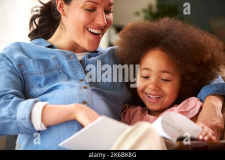 Mère enceinte et fille se détendant sur un canapé à la maison lecture livre ensemble Banque D'Images