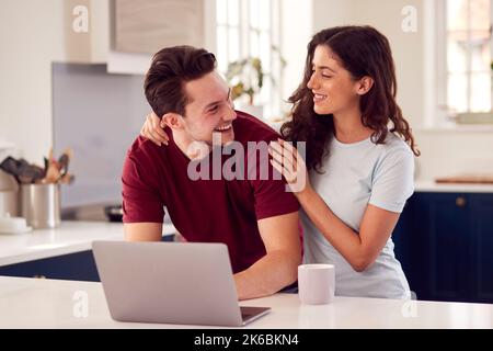 Couple transgenre aimant à la maison regardant ensemble l'ordinateur portable sur le comptoir de cuisine Banque D'Images