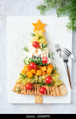 Assiette à fromage en forme d'arbre de Noël avec craquelins, raisins, fromage, tomates et sauce aux canneberges, encas des fêtes d'hiver. Vue de dessus Banque D'Images