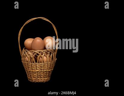 Image d'œufs de poulet dans un panier en osier sur fond noir Banque D'Images