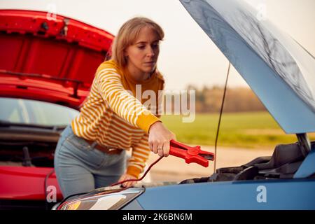 Femme qui fixe le câble volant pour démarrer le moteur de la voiture avec une batterie à plat Banque D'Images