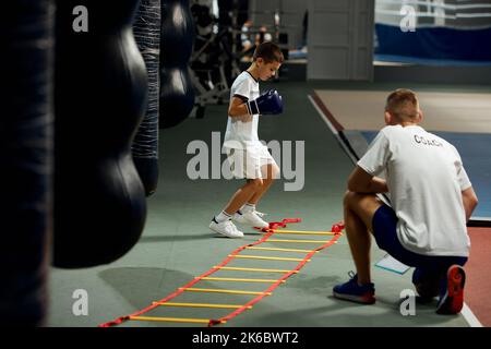 Petit garçon, débutant boxer entraînement avec entraîneur personnel à la salle de sport, à l'intérieur. Concept d'étude, défis, sport, passe-temps, compétition Banque D'Images