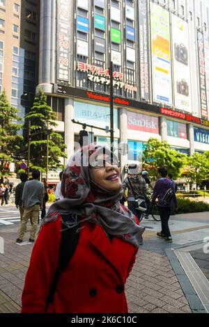 Portait de jeune femme musulmane souriant avec le bâtiment Yodobashi-Akiba et la foule de personnes marchant dans Akihabara et ciel bleu clair. Banque D'Images