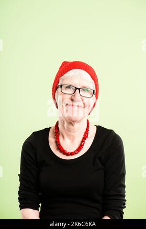 J'ai toujours aimé une touche de couleur. Une femme âgée assise seule dans le studio et posant tout en portant un bonnet. Banque D'Images