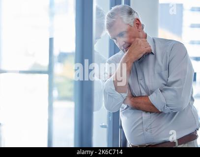 Je crains toujours pour l'avenir de mon entreprise. Un homme d'affaires mature qui regarde stressé tout en se tenant debout devant une fenêtre dans un bureau. Banque D'Images