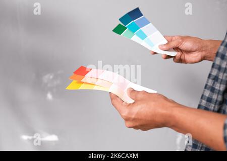 Gros plan des mains tenant les échantillons de peinture de couleur vive contre le mur gris Banque D'Images