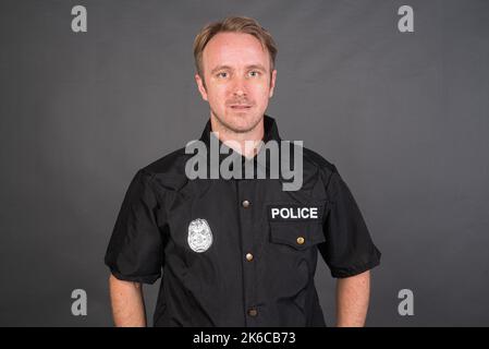 Portrait d'un homme de race blanche portant un costume de police sur fond gris de studio Banque D'Images